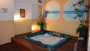 A spa room with a hot tub, wooden flooring, a mural of a beach, and potted plants. - Hotel Ladina (Campitello di Fassa)