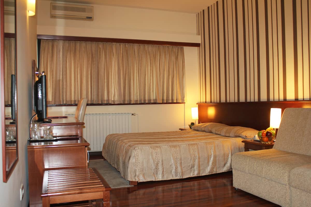 Quarto de hotel com duas camas, uma escrivaninha de madeira, televisão e mesa de cabeceira com luminária e fruteira.