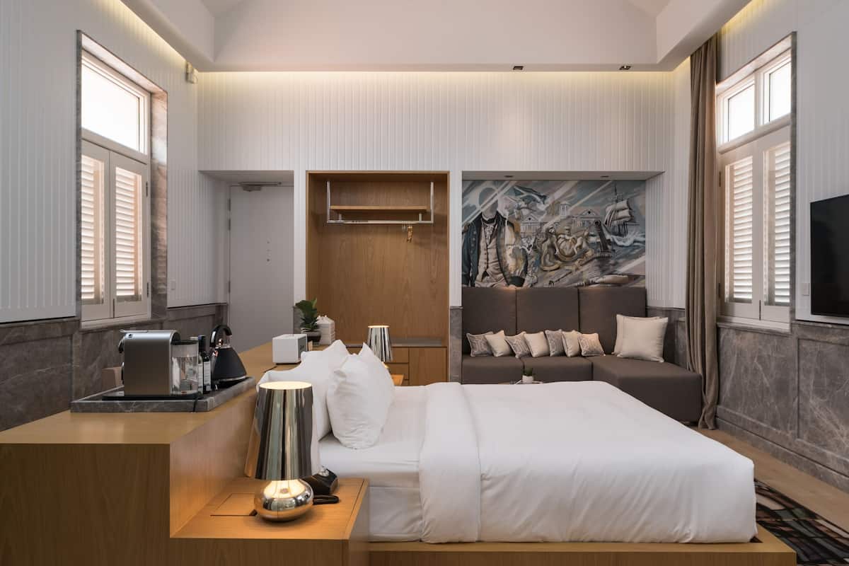 A modern hotel room with a large bed, a desk with a coffee machine, a mural on the wall, and a unique ceiling light fixture.