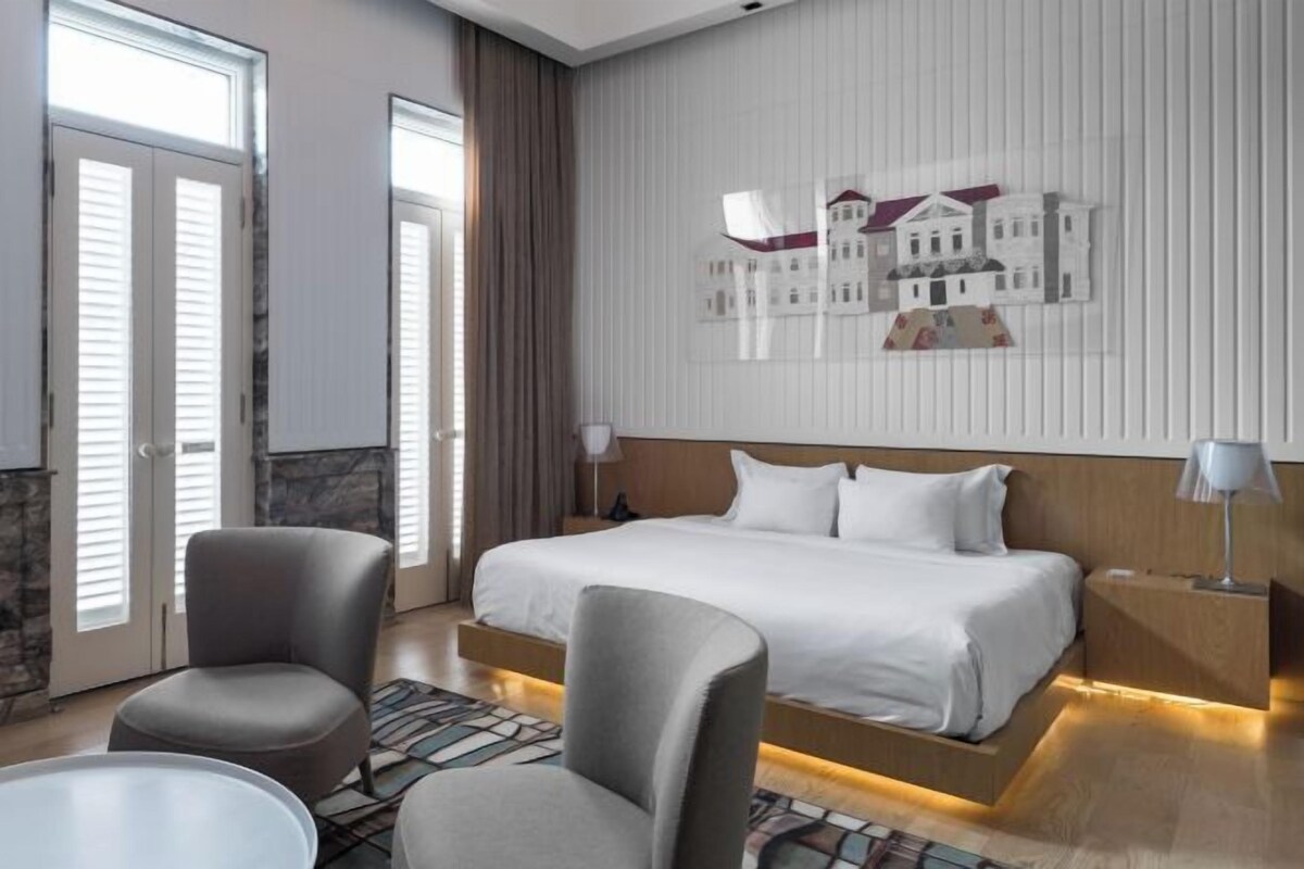 Una camera d'albergo con un letto, due poltrone, un tavolino e un'opera d'arte appesa al muro.
