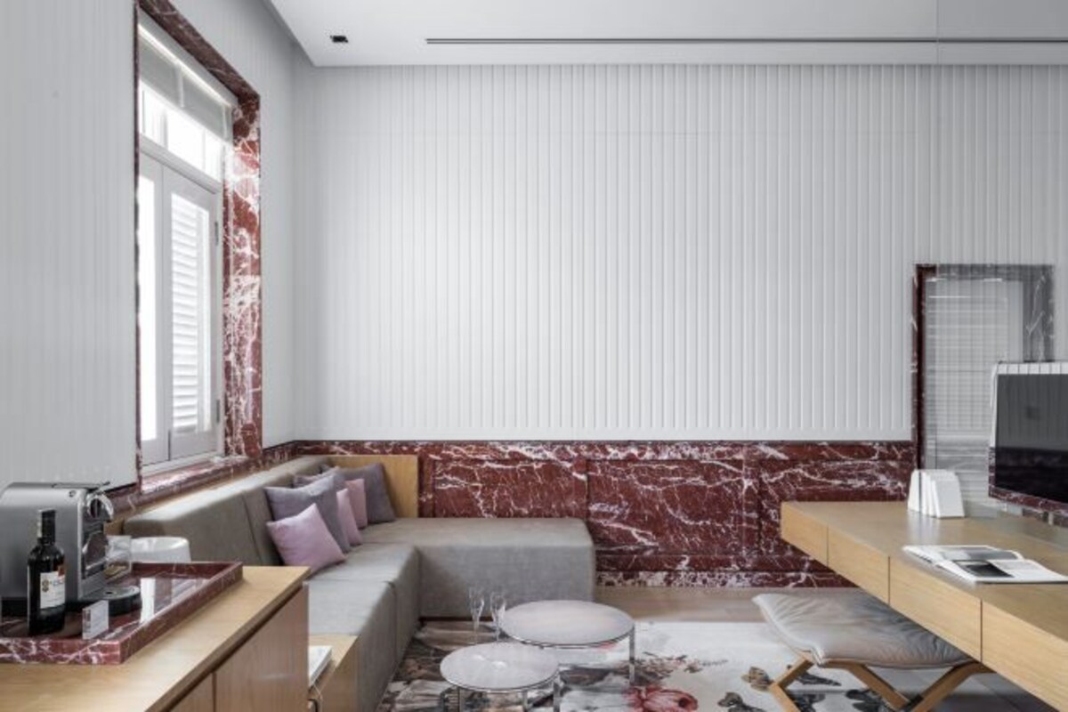 A modern hotel room with a sofa, a desk, a television, and a window with blinds.