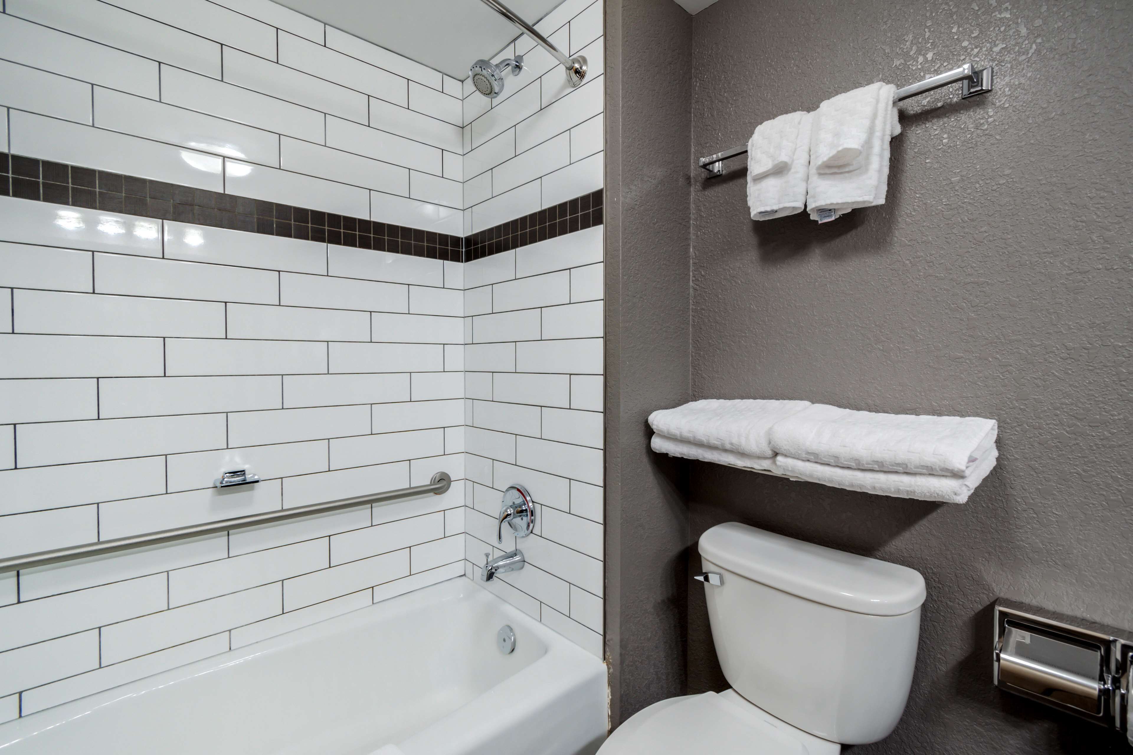 A bathroom with white tiled walls, a white bathtub, a toilet, and a towel rack with towels.
