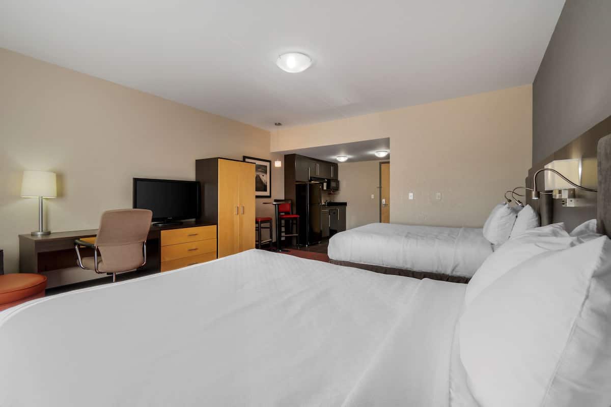 Habitación de hotel con dos camas, un escritorio con silla, televisor y kitchenette.