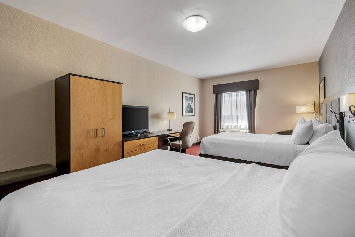 Habitación de hotel con dos camas, un escritorio con televisor, un armario y una ventana con cortinas.