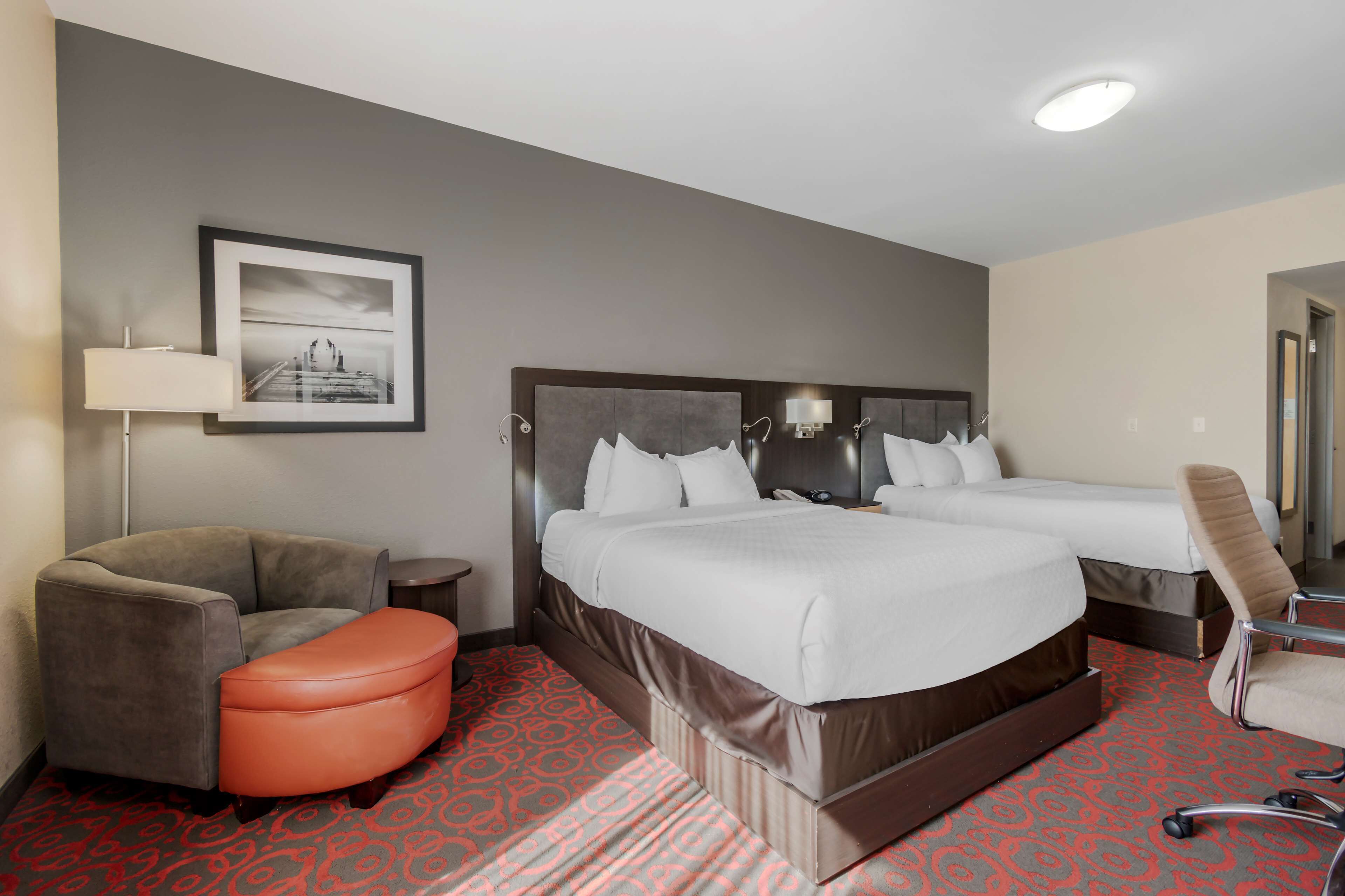 A hotel room with two beds, a sofa, a chair, a lamp, and a framed picture on the wall.