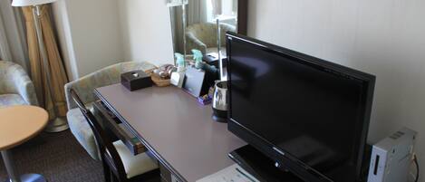 A hotel room with a desk, a television, a computer, and a chair.
