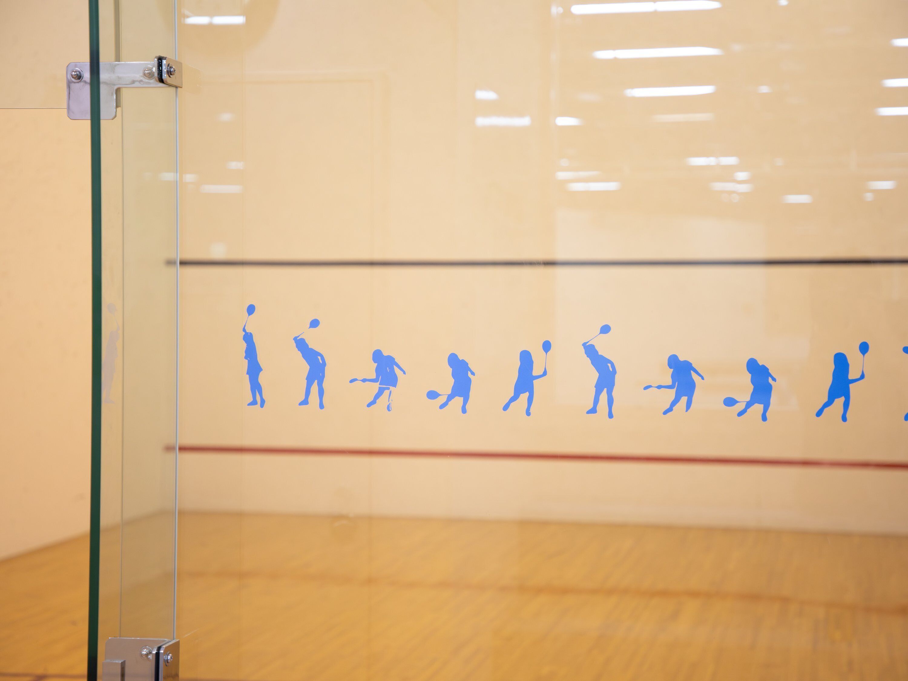 A squash court with a glass wall and a wooden floor.