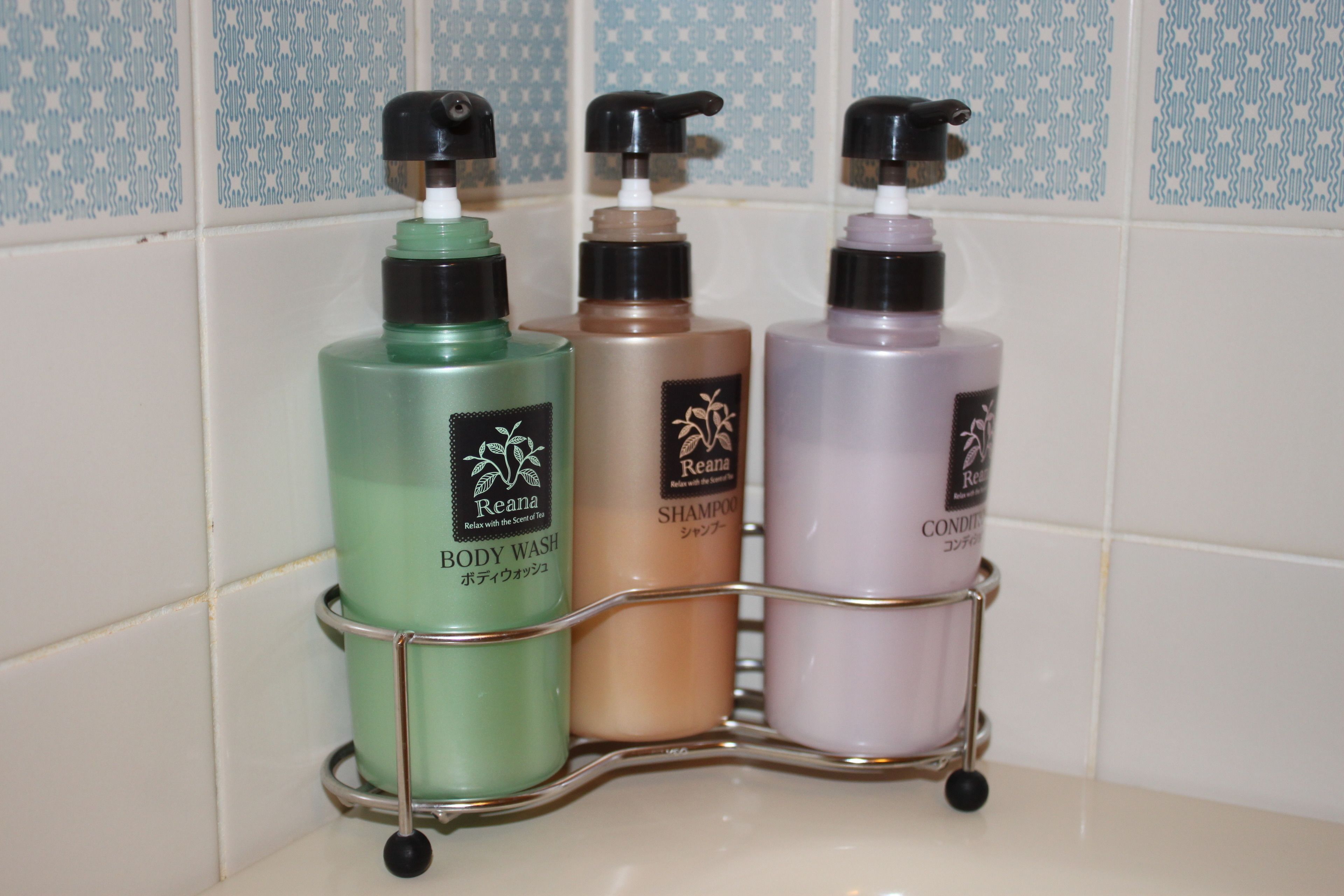 A bathroom shelf with three bottles of Reana body wash, shampoo, and conditioner.