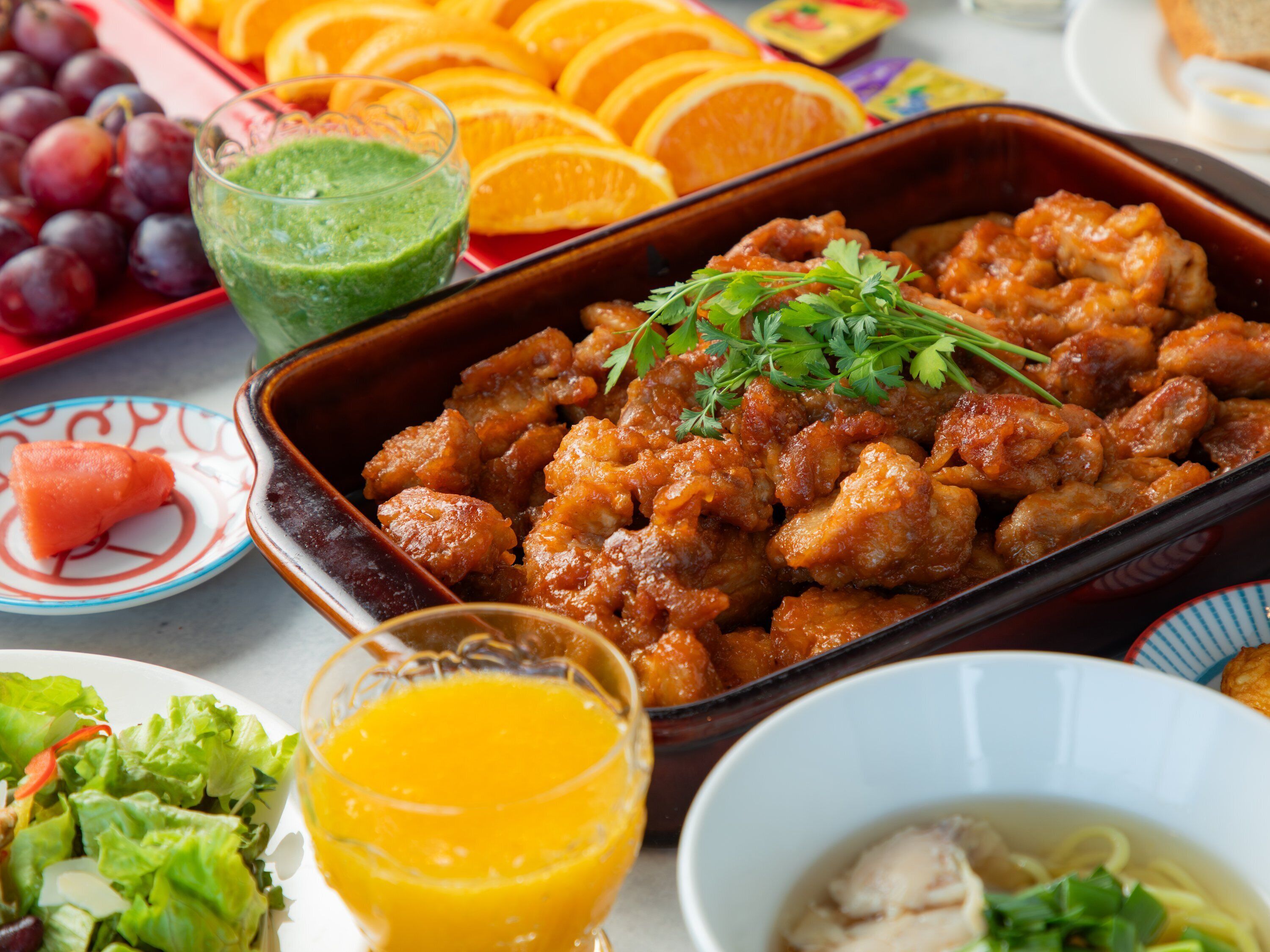 Variedad de platillos, entre ellos un pastel de carne, frutas frescas y un vaso de jugo.
