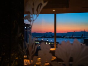 A view of a harbor at dusk with cranes and a bridge, through a window with a plant in the foreground. - Hotel Resol Hakodate (Hakodate)