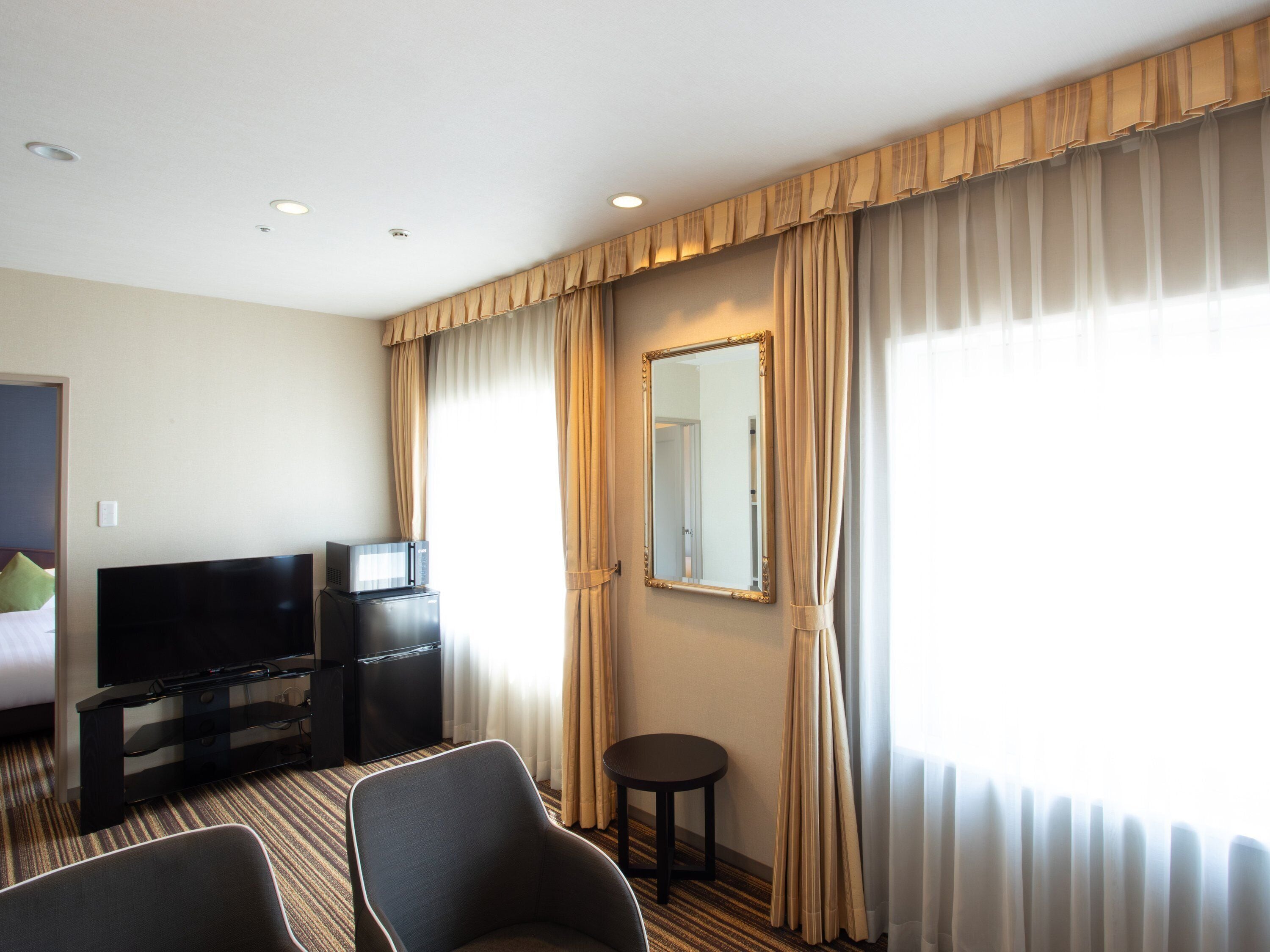 A hotel room with a bed, a television, a minibar, a desk, and a chair.