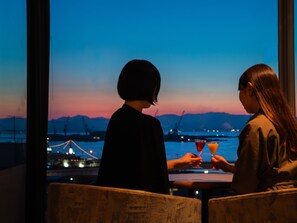 Two individuals seated at a table with a view of a sunset over water and mountains. - Hotel Resol Hakodate (Hakodate)
