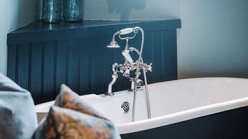 Une baignoire équipée d’une pomme de douche et d’un robinet, d’un drain et d’un mur bleu foncé avec un lambris vertical.