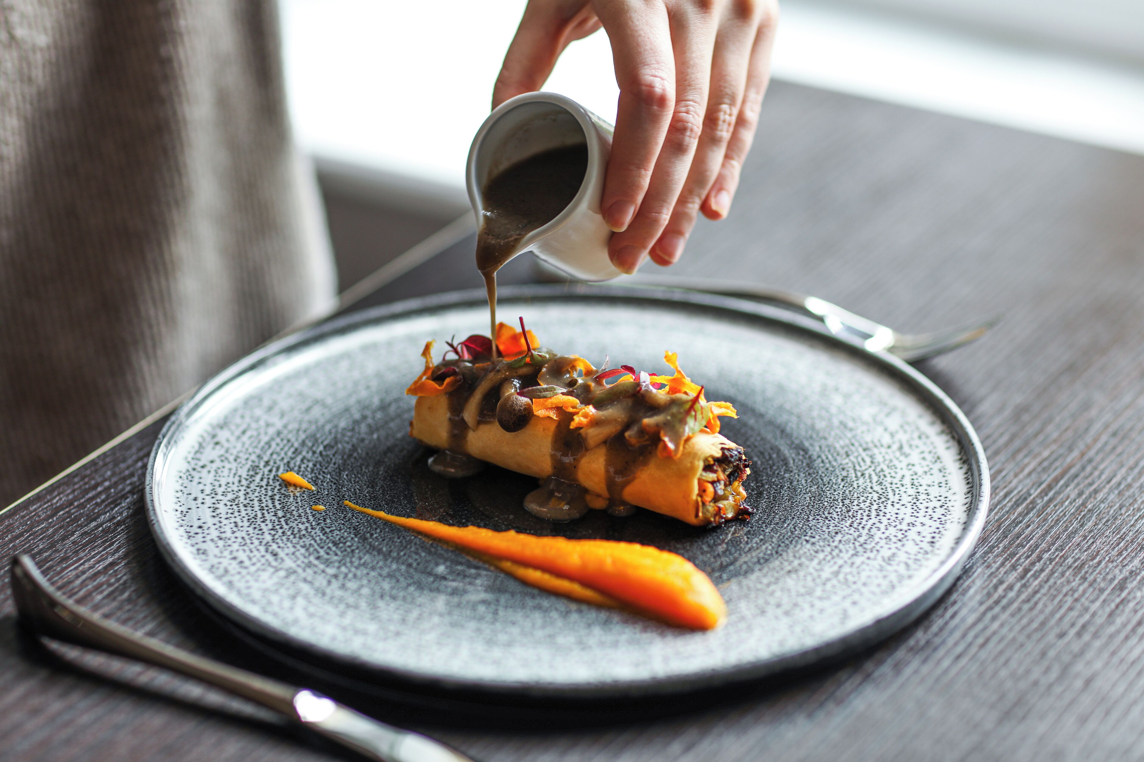 A person pouring sauce onto a dish on a plate.