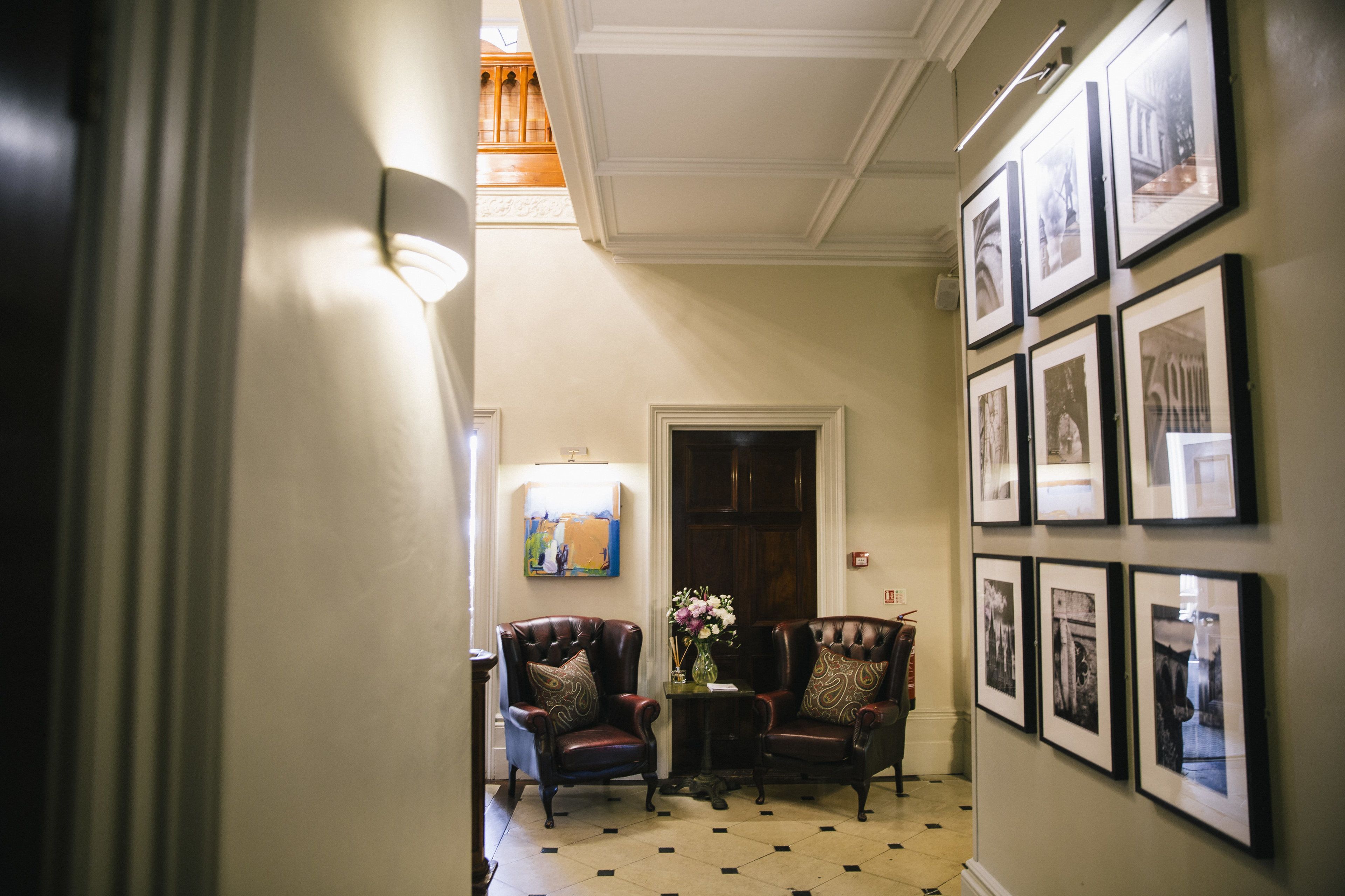 A hallway with two leather armchairs, a vase with flowers, and framed pictures on the wall.