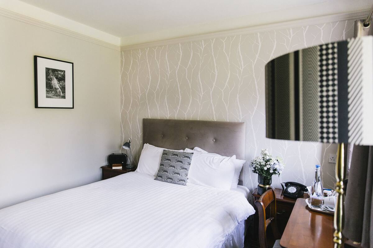 Un lit bien fait, avec du linge de lit blanc, une tête de lit grise et un tableau encadré accroché au mur.