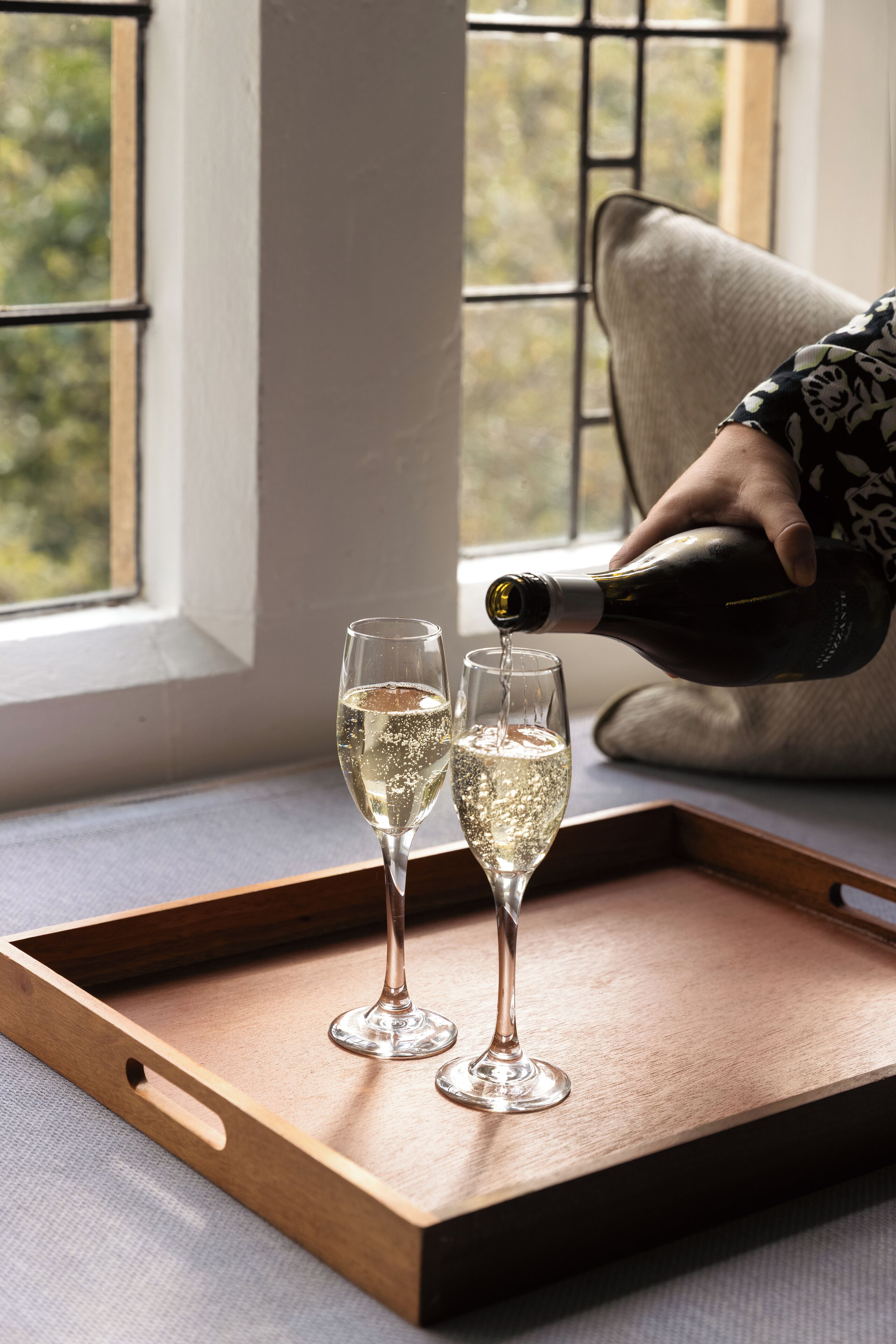 A wooden tray with two glasses of white wine on a windowsill.