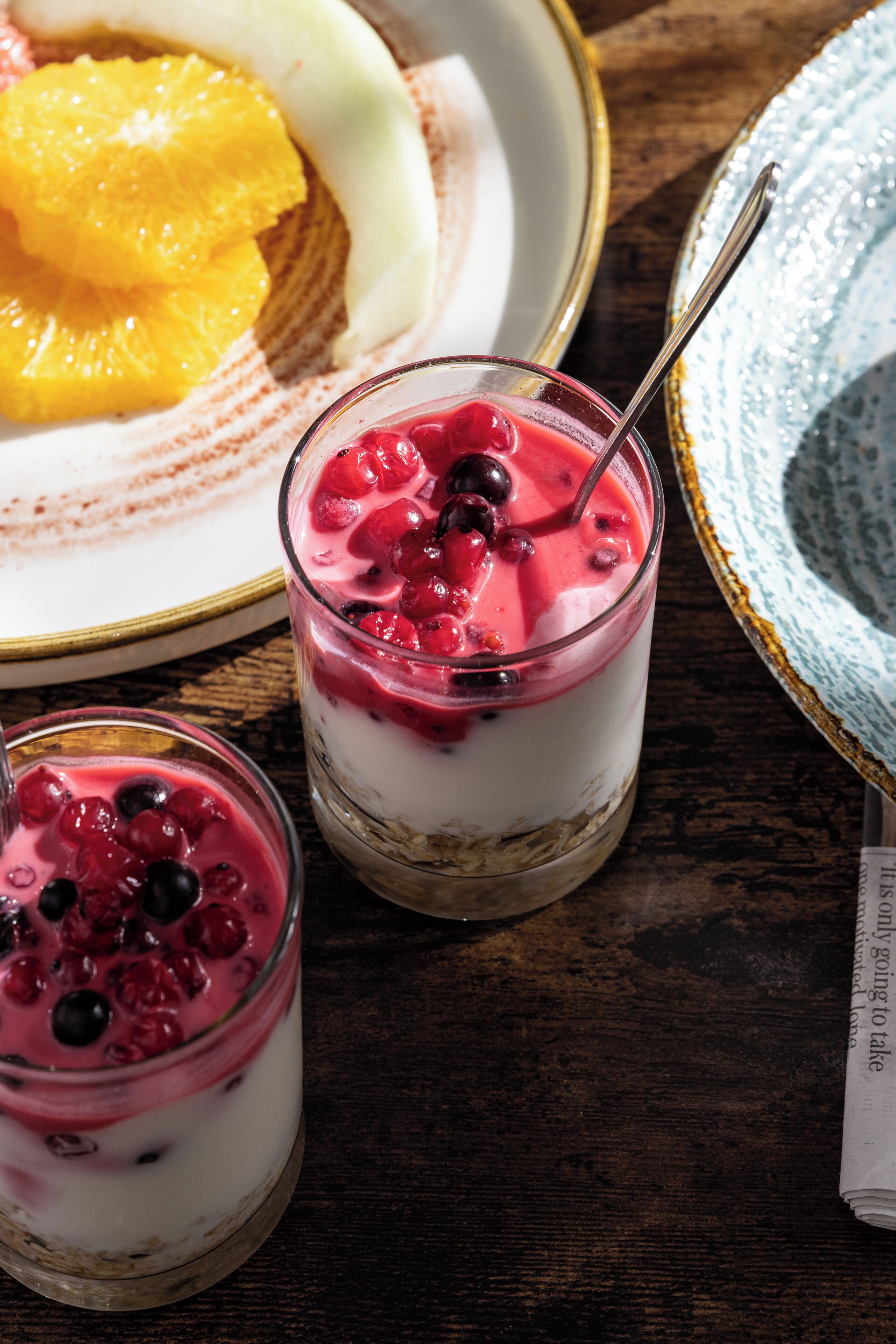 A dessert setting with layered parfaits and fresh fruits on a wooden table.