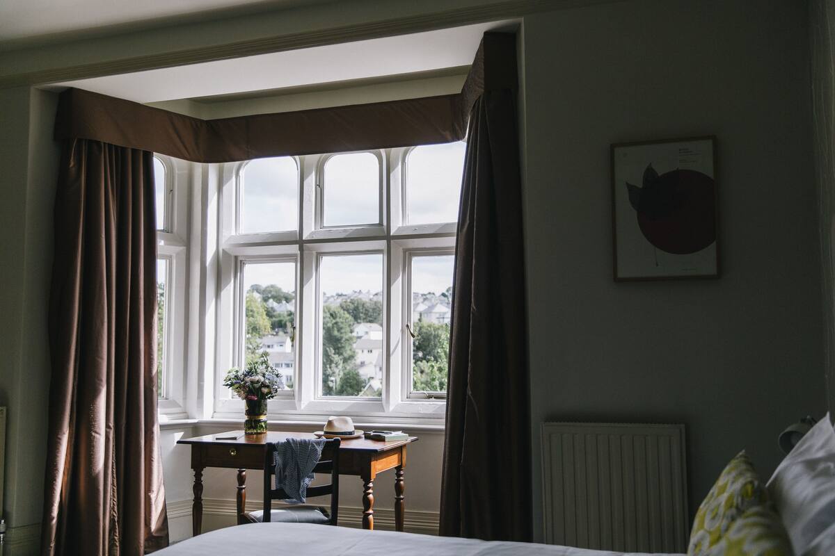 Une chambre avec une grande fenêtre, une table de chevet, une chaise, un radiateur et un lit.