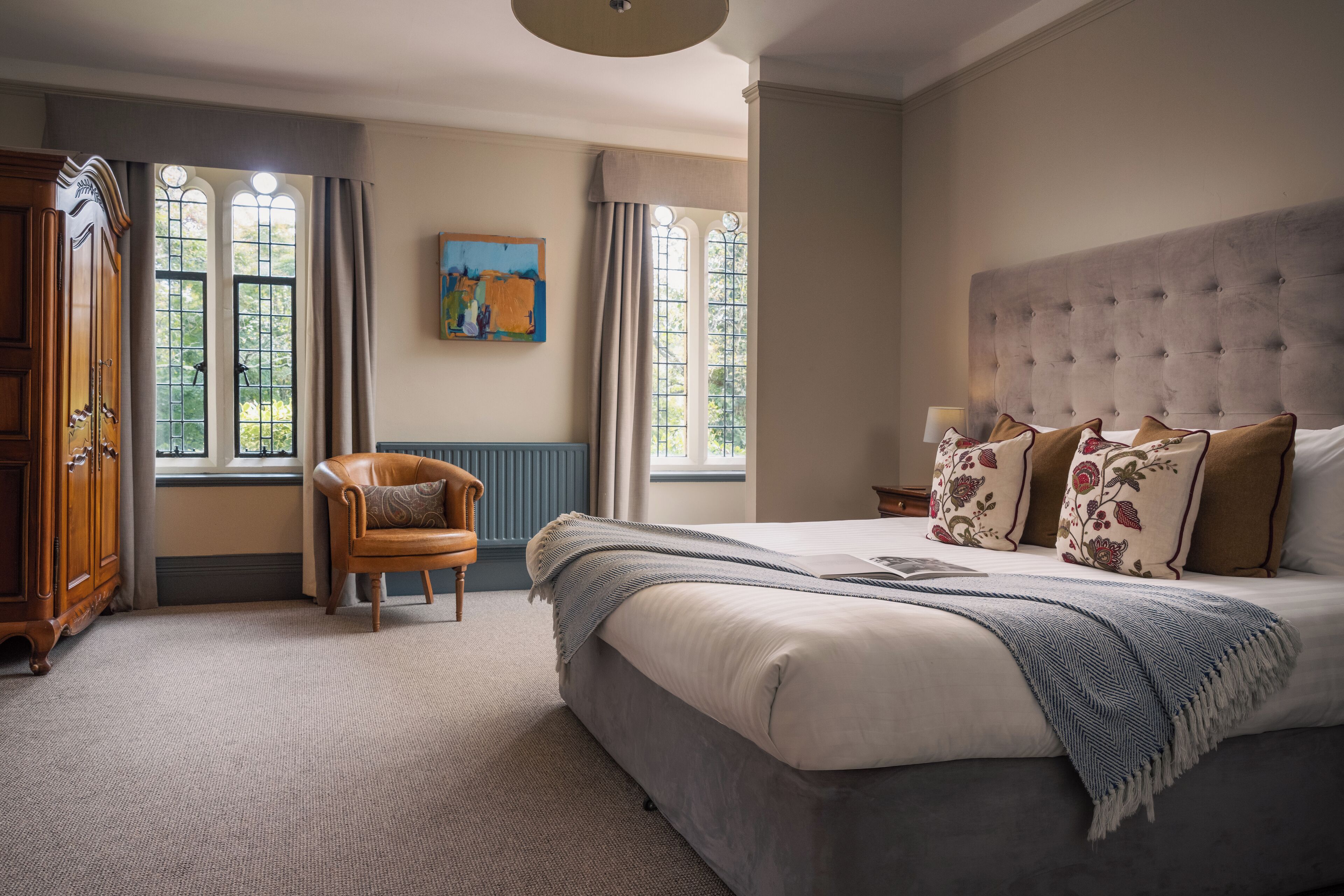 A bedroom with a large bed, a wooden wardrobe, a chair, and a painting on the wall.