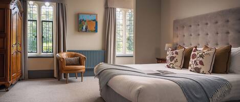 A bedroom with a large bed, a wooden wardrobe, a chair, and a painting on the wall.