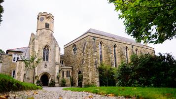 A historic stone building with a prominent tower and arched windows, surrounded by greenery.