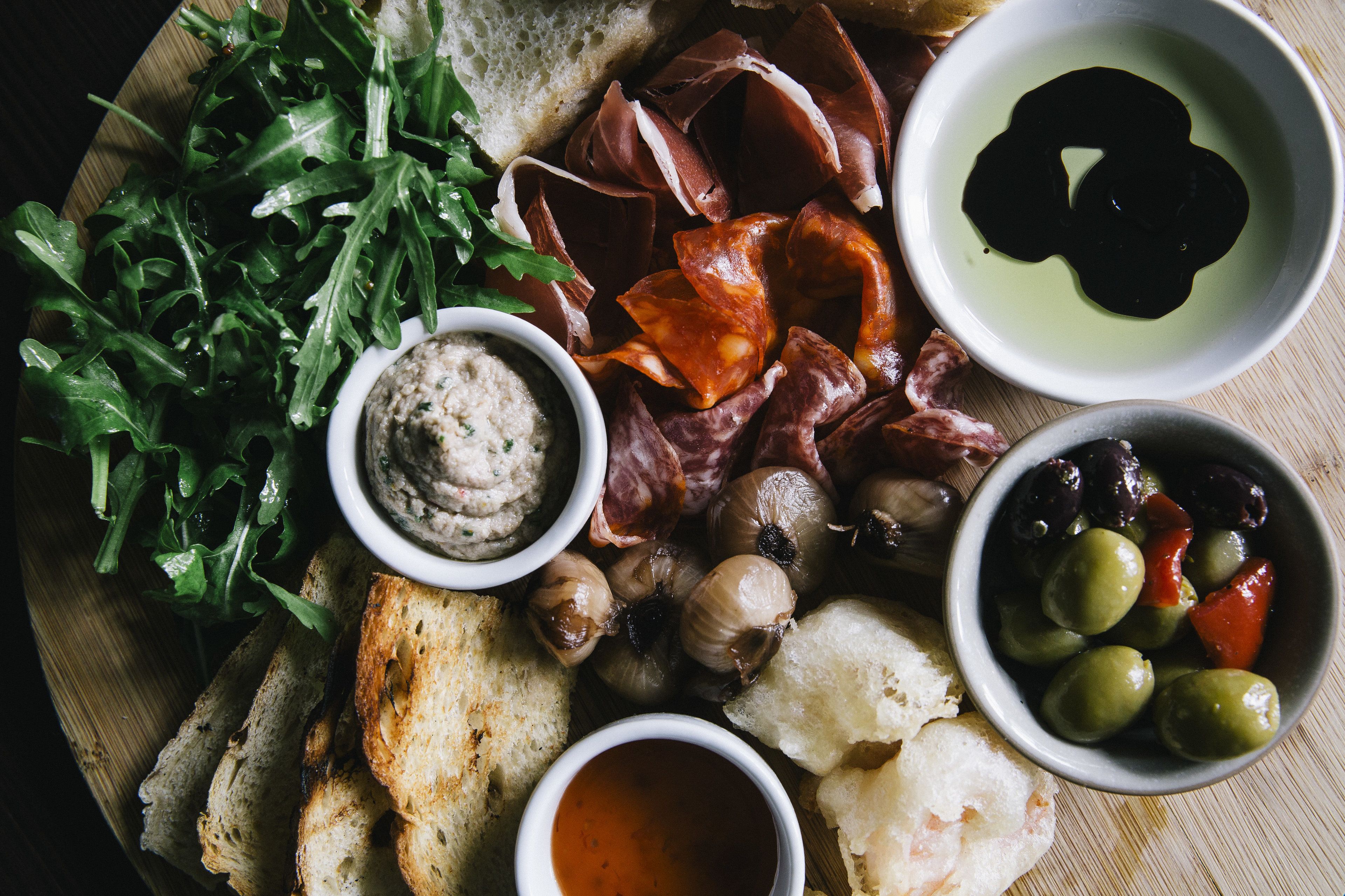 A charcuterie board with various meats, olives, bread, and dips.