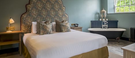 A bedroom with a large bed, a vintage telephone, a bathtub, and a window with a view of greenery.
