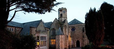 A historic stone building with a clock tower, arched windows, and a gated entrance.