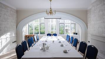 Ein Konferenzraum mit langem Tisch, blauen Stühlen, einer weißen Tischdecke und einer Kristallleuchter.
