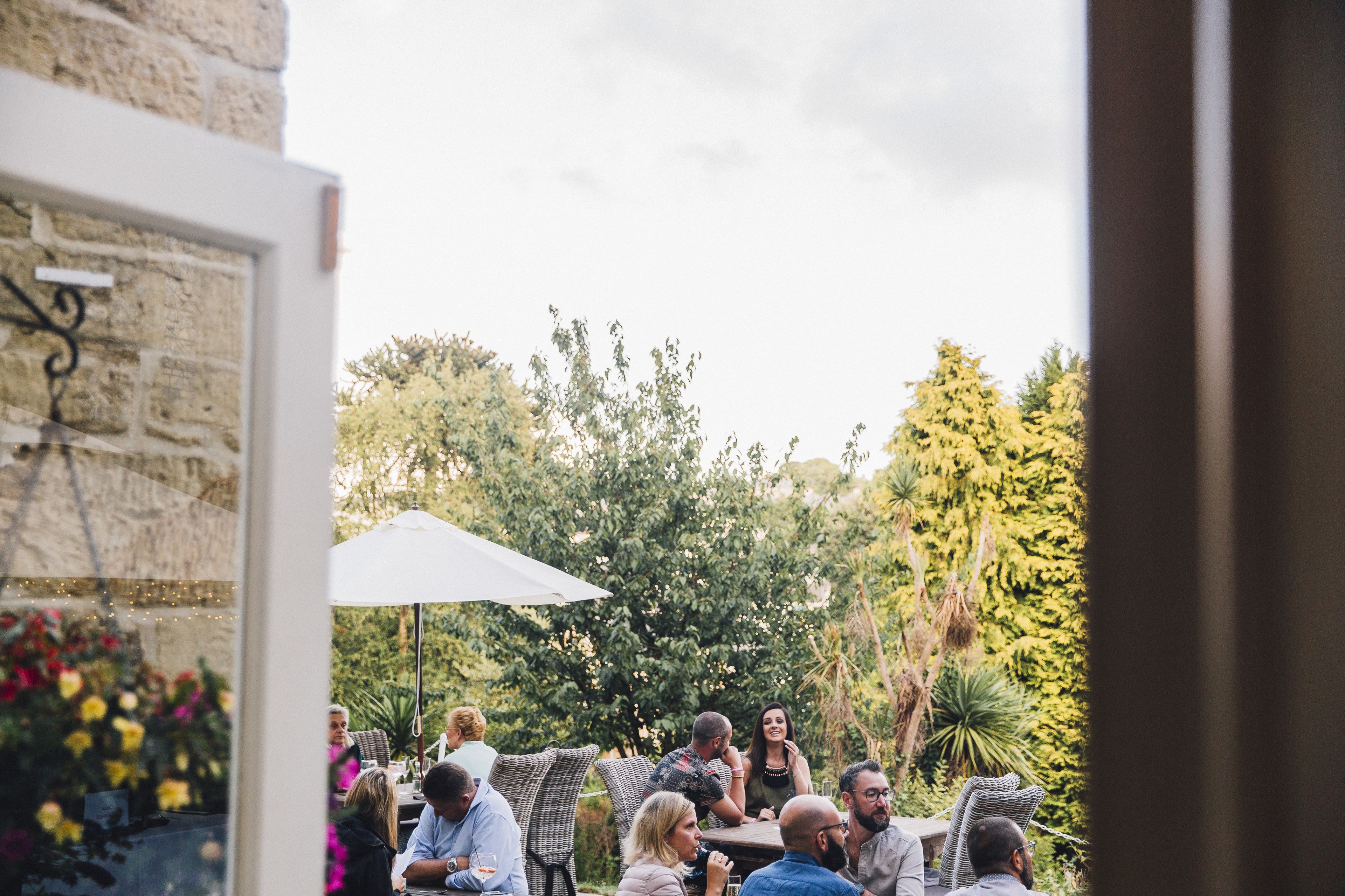 An outdoor seating area with tables and chairs, surrounded by greenery and trees.