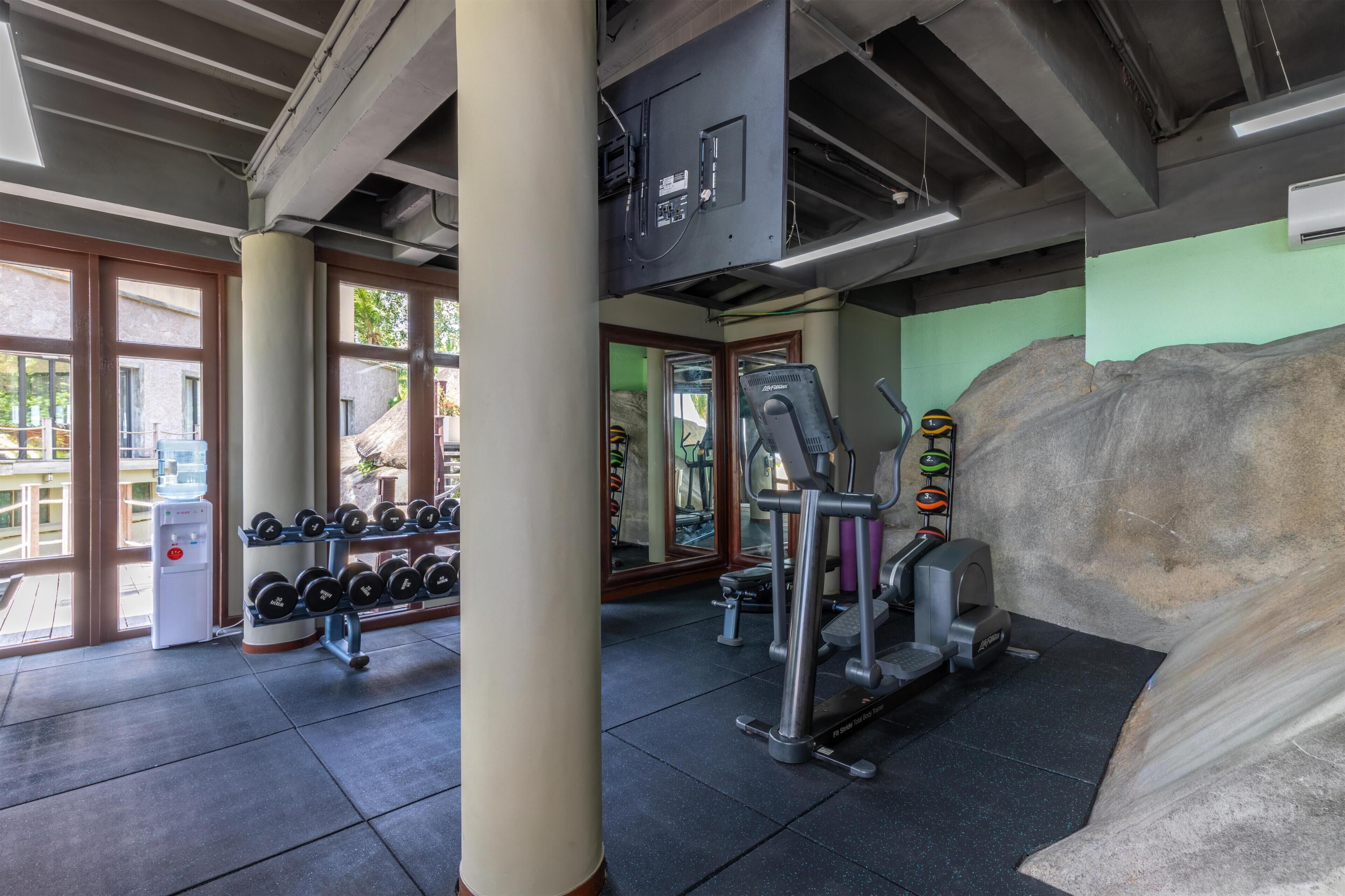 A gym with exercise equipment, a water dispenser, and large windows.