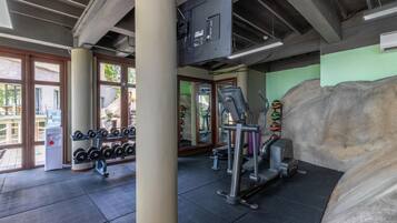 Un gimnasio con equipo de ejercicio, dispensador de agua y ventanas amplias.