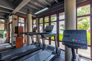 A gym with treadmills, a digital workout station, and large windows with a view of palm trees.
