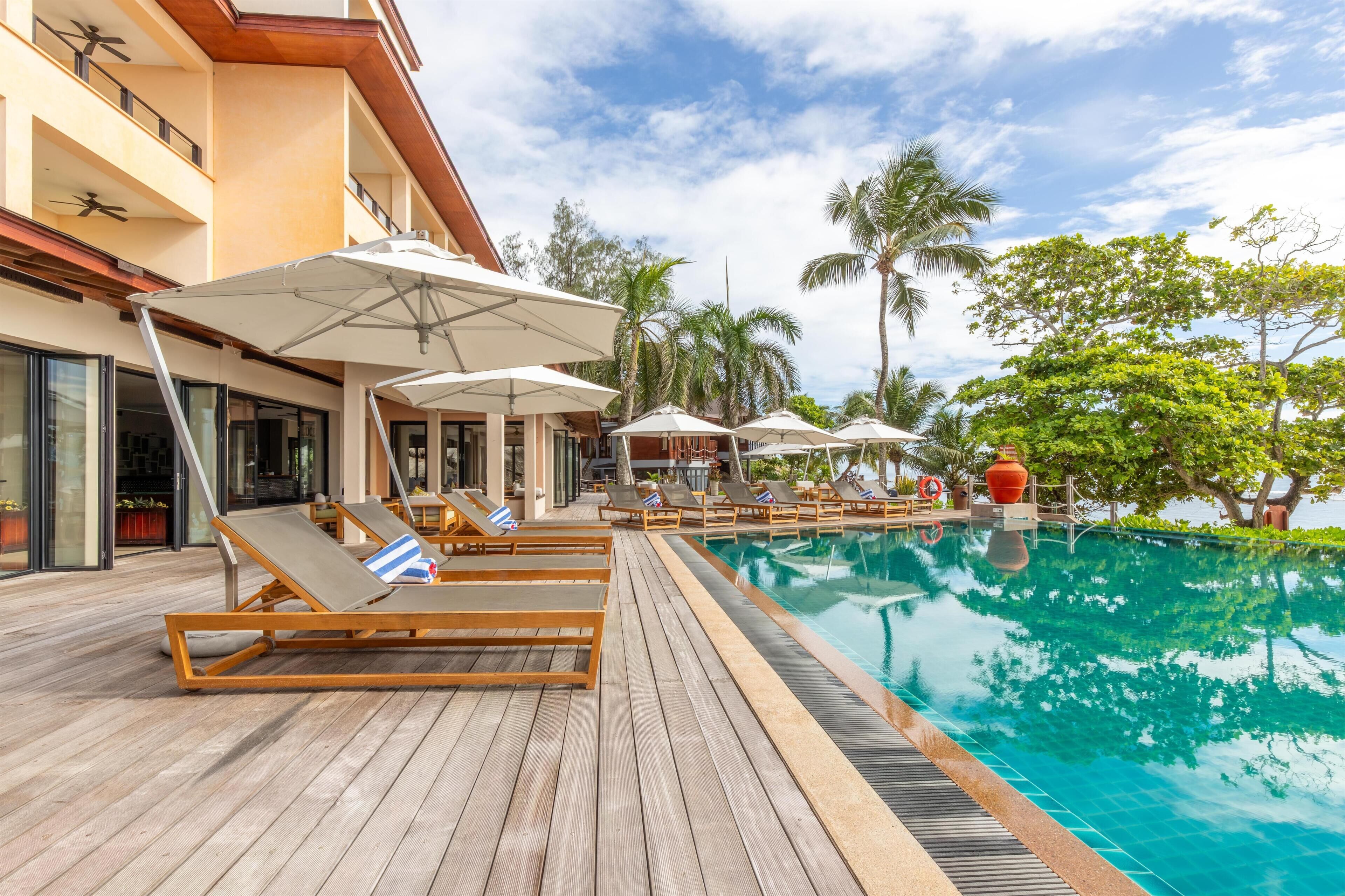 A poolside area with lounge chairs and umbrellas, a wooden deck, and a clear blue pool.