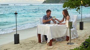 Una pareja cenando en una mesa en la playa, con vistas al océano.
