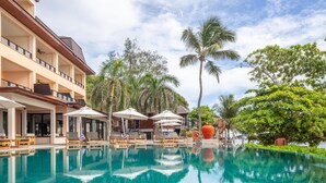 Un hotel con piscina, sillas de descanso, sombrillas y palmeras.
