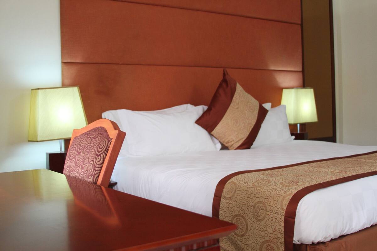 A hotel room with a large bed, two bedside tables, and two lamps.