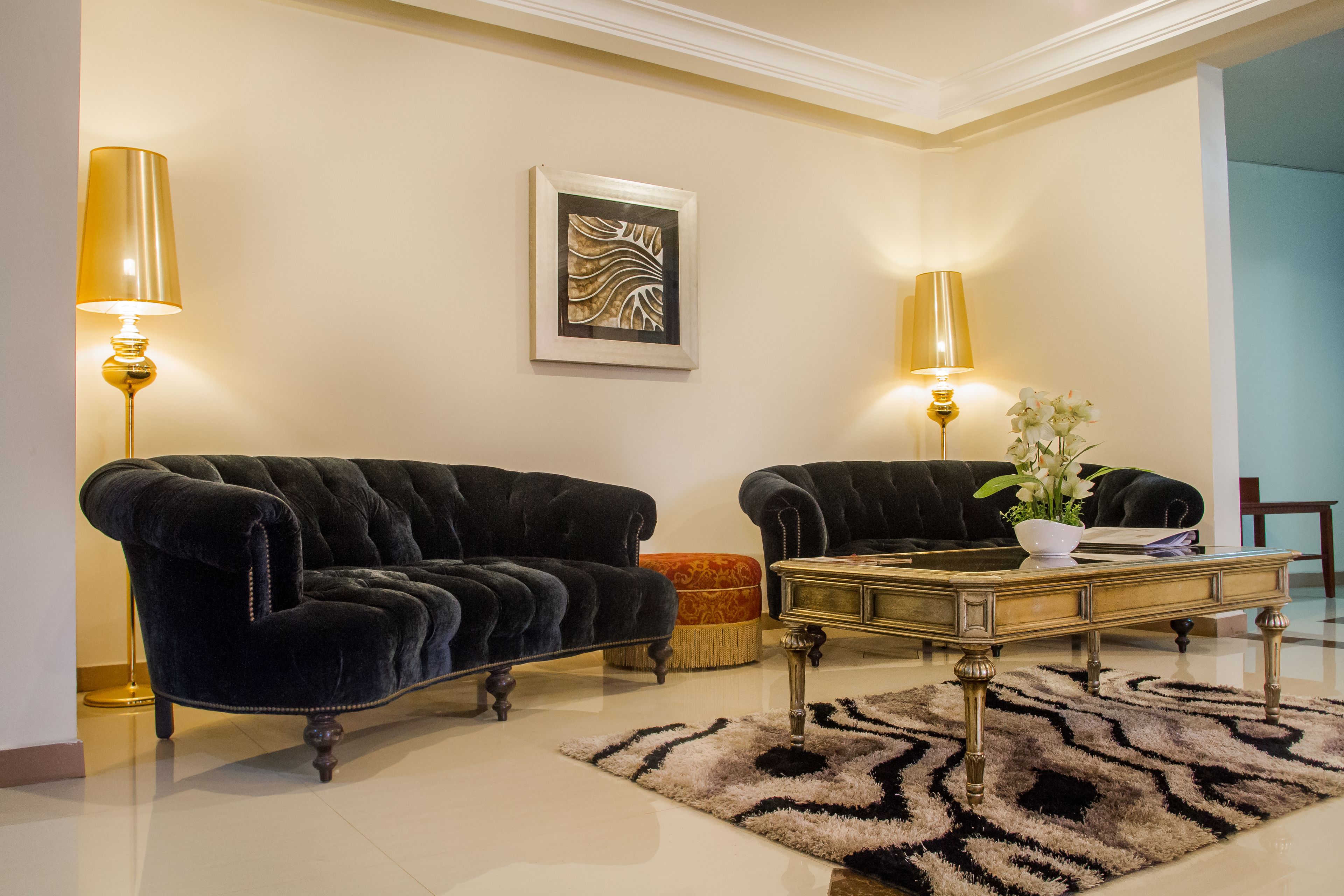 A living room with two black velvet sofas, a glass coffee table, and two lamps.