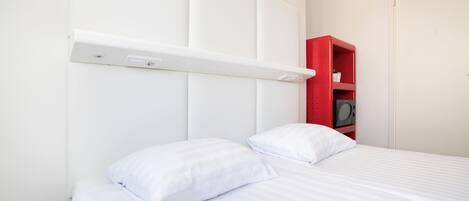 A neatly made bed with white bedding and pillows, a white headboard, and a red shelf unit with a speaker.