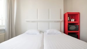 A hotel room with a bed, white curtains, a red shelf with a microwave, and a white headboard. - Omena Hotel Jyväskylä (Jyväskylä)