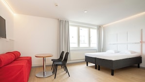A modern hotel room with a bed, a red sofa, a small round table, and two black chairs. - Omena Hotel Jyväskylä (Jyväskylä)