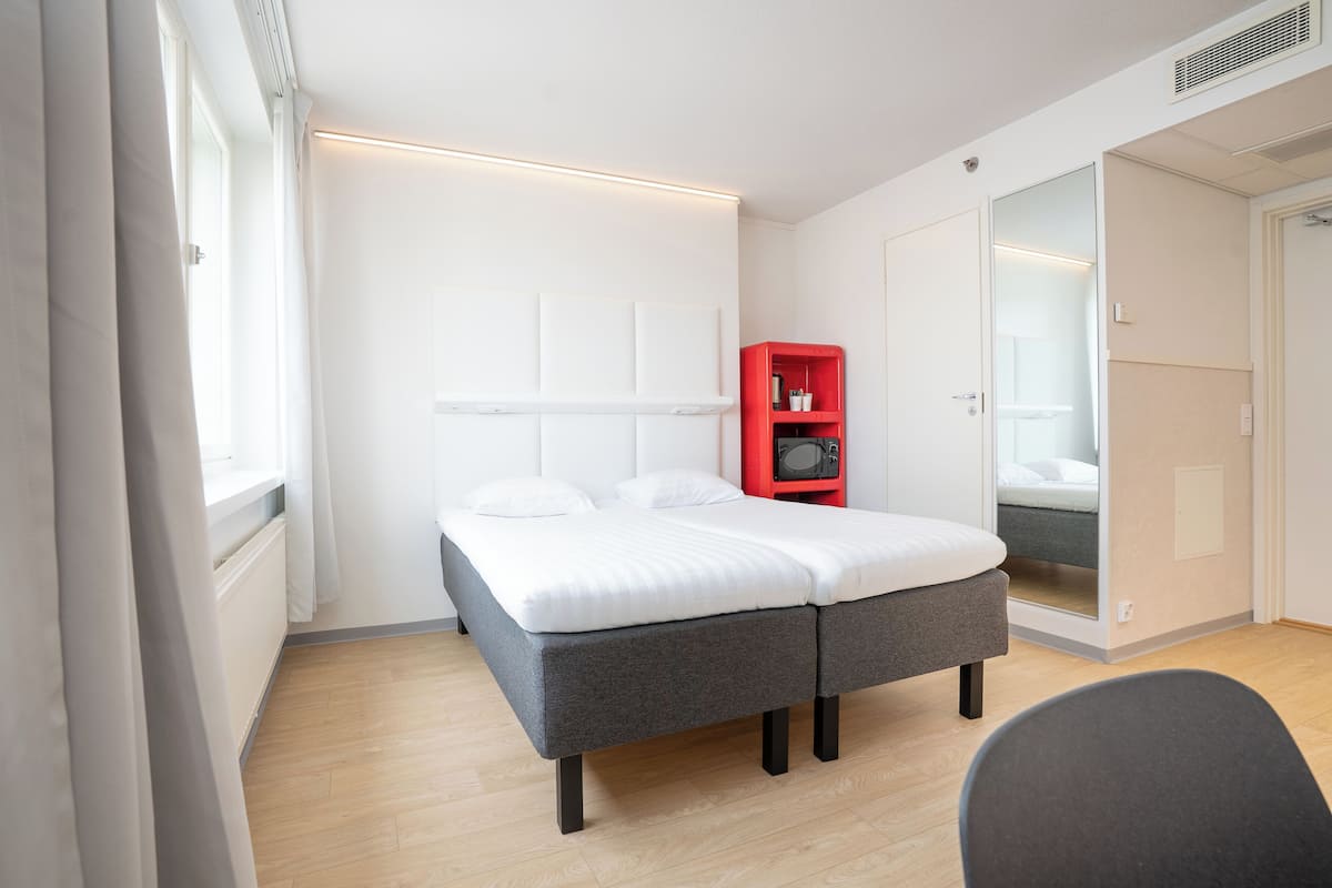 A modern bedroom with a bed, a red storage unit, and a mirror.
