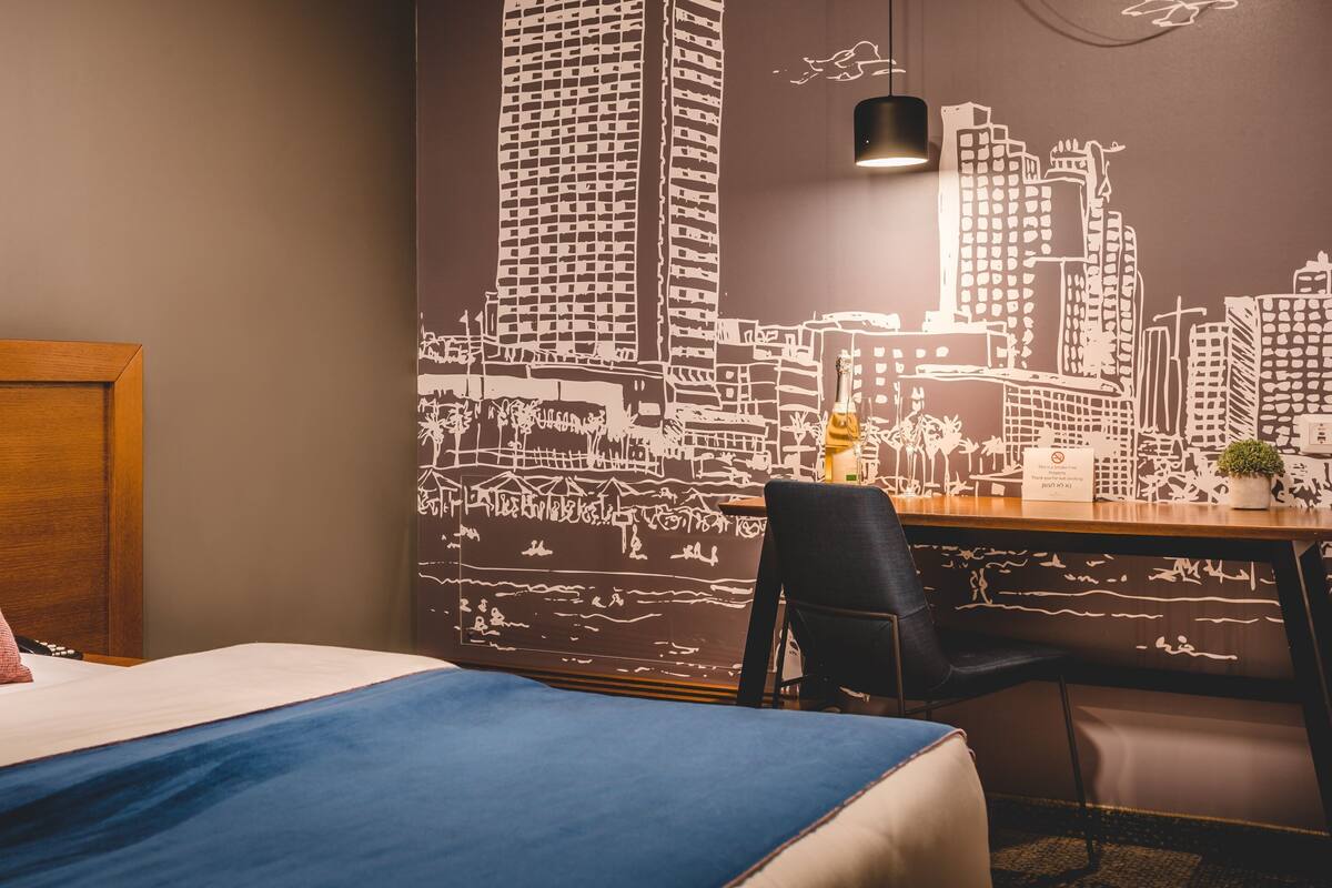 Habitación de hotel con cama, escritorio y un mural con vista a la ciudad.