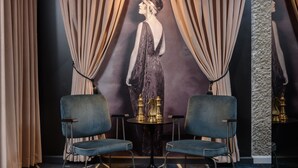 Une pièce avec deux chaises bleues, une petite table ronde sur laquelle se trouvent des salières et des poivrières, et un grand tableau représentant une femme accroché au mur.