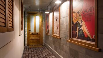 A hallway with a cobblestone floor, wooden doors, and framed posters on the walls.