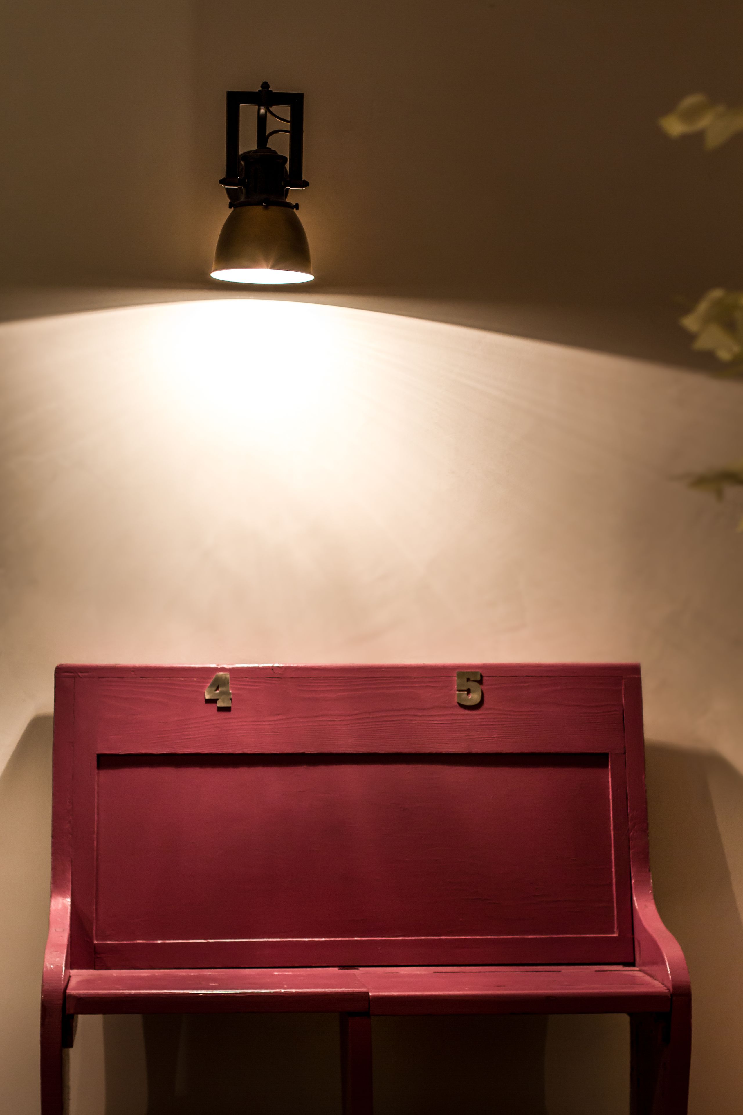 Un banc rouge doté d’un cadenas à chiffres, placé sous un luminaire fixé au mur.