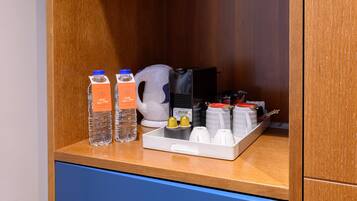 A hotel minibar with bottled water, a coffee maker, and various condiments.
