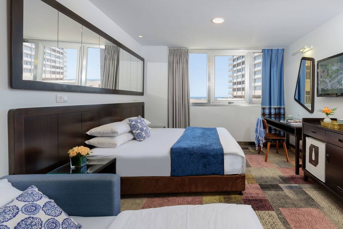 Una habitación de hotel con una cama, un escritorio, una silla, un aparador y un espejo grande.