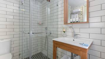 A modern bathroom with white subway tiles, a glass-enclosed shower, a wooden vanity with a sink, and a mirror.